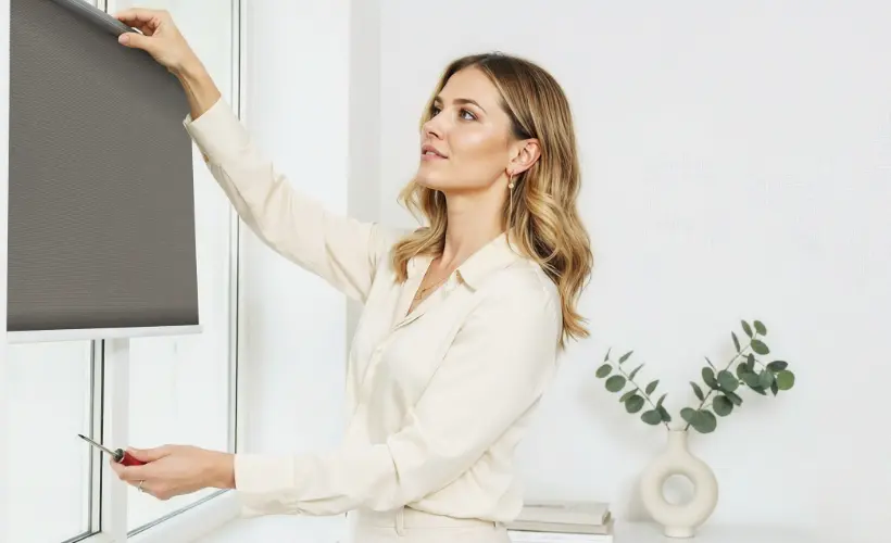 A woman installing a grey fabric roller blind.